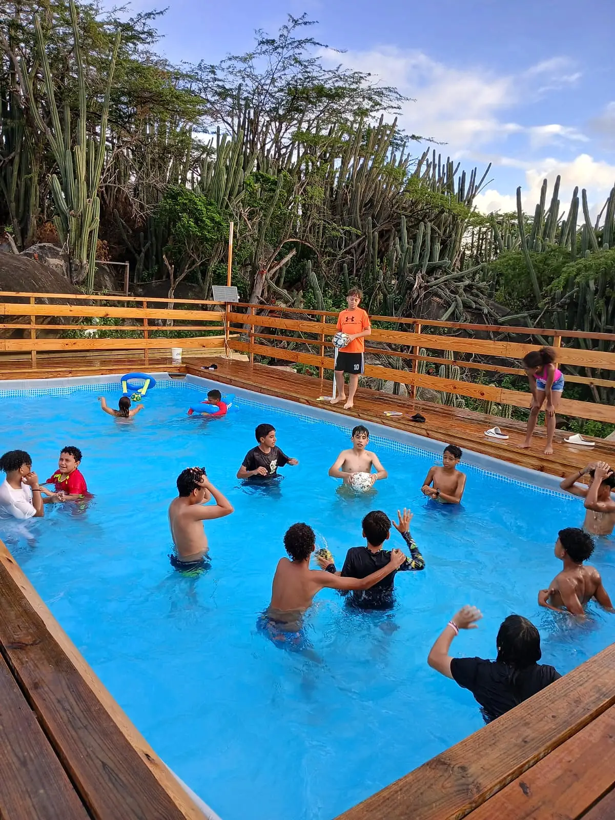 Children playing in the pool, with a wooden deck and cacti behind